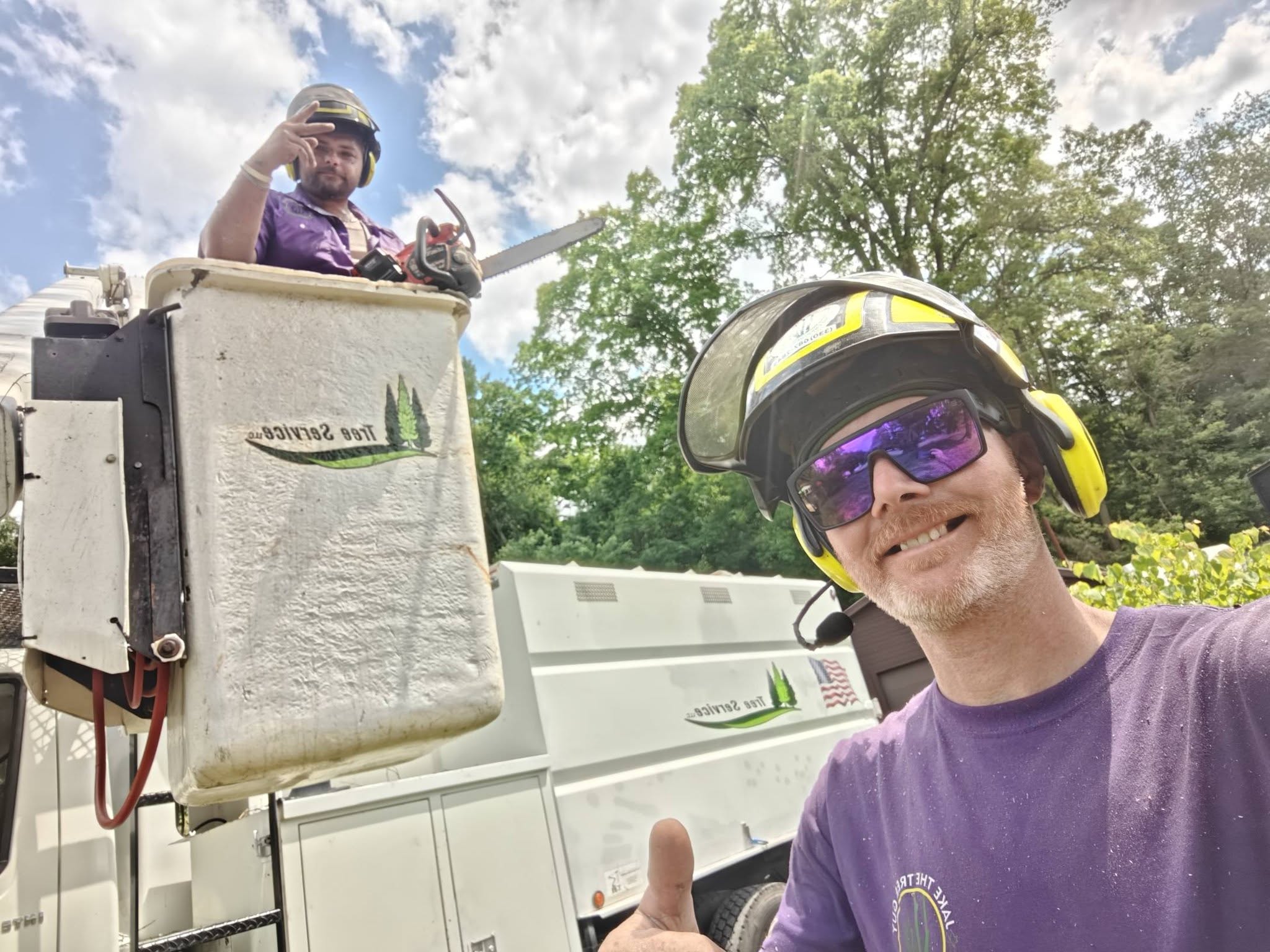 Jake giving thumbs up selfie with crew member operating bucket truck during tree removal