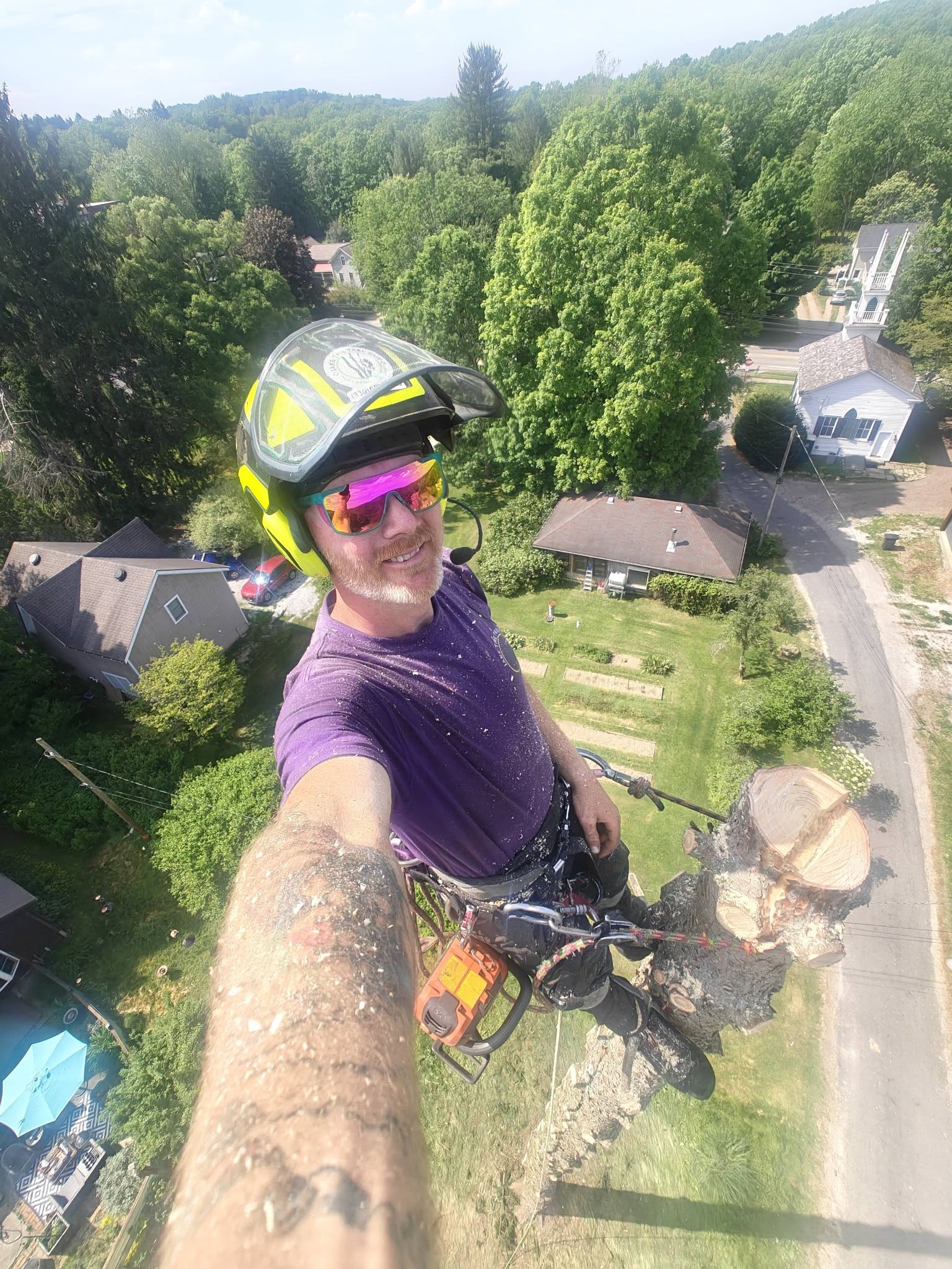Jake selfie at extreme height during tree removal with suburban neighborhood visible far below